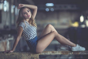 身穿條紋襯衫和牛仔短褲的年輕女性夜間在生鏽壁架上擺姿勢。