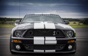 暴風雨天空下，賽道上的黑色 Shelby Mustang 帶有白色條紋。