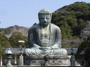 寺廟花園中的大型青銅佛像，背景有樹木和山脈。