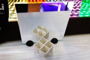 白色幾何3D打印物體和黑色蓋子放在木質表面上，鏡子中反射出多彩的LED燈光。