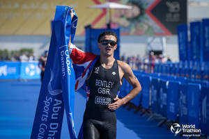 三項鐵人運動員 Bentley GBR 在阿布扎比世界三項鐵人賽中手持旗幟和橫幅慶祝勝利。 — 跑步 壁紙