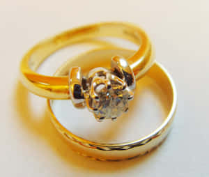 兩枚金結婚戒指，一枚鑲有單鑽，交纏在白色表面上