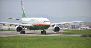 綠色和白色的長榮航空飛機在機場跑道滑行，背景有山脈。