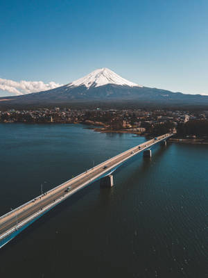 一座橋橫跨湖泊，遠處的富士山在清澈的藍天下。
