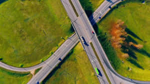 從高空俯瞰被綠色山丘和秋樹環繞的高速公路交匯處。 — 道路 壁紙
