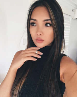 擁有長長黑髮和濃妝的女性，穿著黑色高領毛衣和銀戒指的室內照。