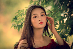 一位身穿紅色連衣裙的女性站在金色陽光下的綠葉之間。