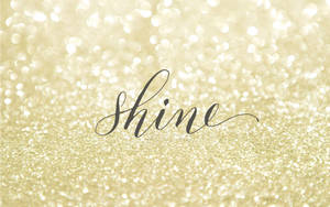喺金色閃粉背景上以草書寫嘅「shine」呢個詞。