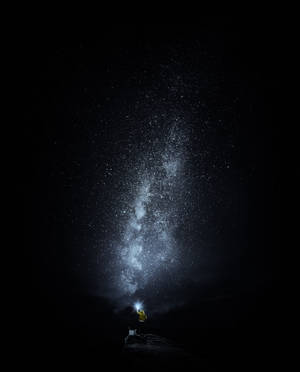 穿黃色外套的人晚上用手電筒照射銀河星星。