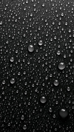 黑色表面上反射光線的雨滴特寫。 — 黑色 iPhone 壁紙