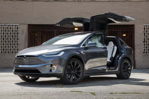 深灰色 Tesla Model X 展開鷹翼門，停在磚砌建築前。
