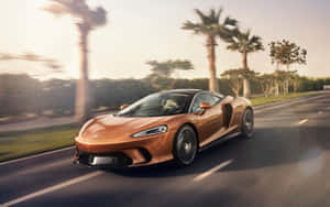 銅色McLaren跑車在日落時分在棕櫚樹成蔭的道路上疾馳。