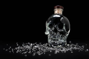 骷髏形玻璃瓶配木蓋，被玻璃碎片環繞在黑色表面上。