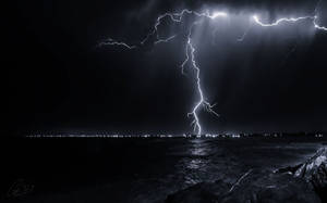 閃電照亮夜間暴風雨的海洋，遠處有城市燈光。