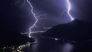 閃電劃過黑暗的湖面，沿岸有城市燈光。