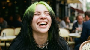 一位頭髮帶有綠色條紋的女子在戶外咖啡館開懷大笑。