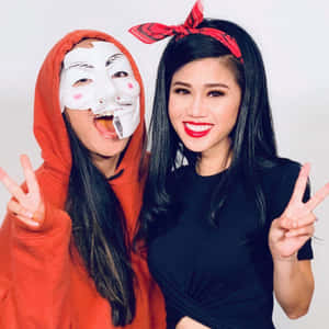兩位女性比出和平手勢，一位穿紅色連帽衫戴面具，另一位穿黑色上衣戴紅色頭巾。
