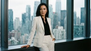 自信的女商人身穿白色西裝站在城市景觀窗前。
