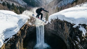 滑雪板運動員在白雪覆蓋的山地景觀中跳躍過瀑布。