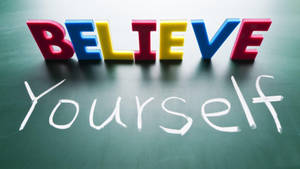 色彩繽紛的3D字母拼出BELIEVE，放在一塊用粉筆寫着'Yourself'的黑板上。