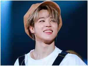 年輕男子戴著棕褐色帽子、穿著白襯衫，在舞台燈光下微笑。 — Jimin GIF 壁紙