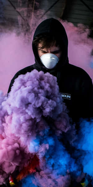 在工業空間中，穿著黑色連帽衫和白色口罩的人置身於彩色煙霧中。 — 淨化面具 壁紙