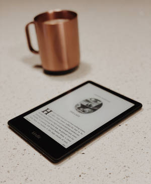 Kindle顯示書頁，旁邊有銅杯，放在有斑點的檯面上。