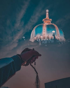 手持念珠在暮色中伸向發光的寺廟圓頂。 — 藍天 壁紙