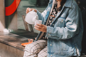 人將白色水壺中的茶倒入杯中，坐在戶外長椅上。 — 青綠色 GIF 壁紙