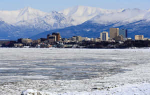 結冰的湖泊與城市和白雪覆蓋的山脈在背景中 — 雪景美學 壁紙