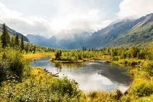 一條河流蜿蜒穿過山谷，周圍是森林覆蓋的山脈，山頂積雪。 — 湖景 壁紙