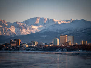 城市天際線與積雪的山峰在日出時倒映在結冰的河流中。 — 城市景觀 壁紙