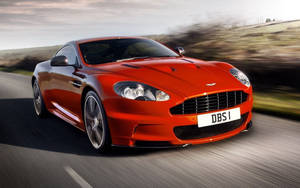 紅色Aston Martin DBS在日落時分在風景優美的道路上疾馳。