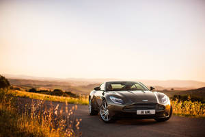 夕陽下風景如畫的鄉村道路上的銀色Aston Martin DB11。