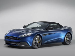 藍色 Aston Martin 開篷車，配備黑色車頂和黃色制動卡鉗，在工作室環境中。
