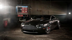 啞光黑色Aston Martin在昏暗的工業車庫中，聚光燈照射。