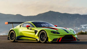 日落時分，青檸綠色 Aston Martin 賽車在賽道上，以山脈為背景。