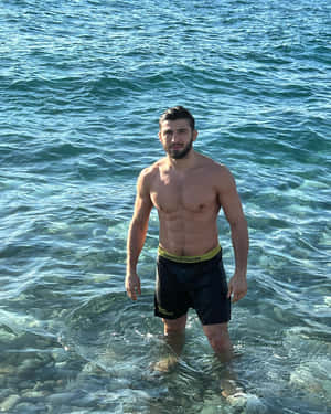 一個健美的男人站在淺海水中，下方岩石可見。 — 水 GIF 壁紙