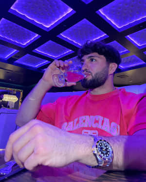 男子在紫色燈光的休息室中飲用粉紅色雞尾酒，身穿粉紅色 Balenciaga 襯衫和奢華手錶。