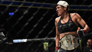 女性MMA拳手在八角籠內手持冠軍腰帶慶祝勝利。