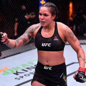 女性MMA拳手在UFC八角籠內慶祝勝利，帶有紋身和手套。