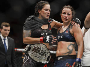 兩名女性MMA拳手在血腥的UFC比賽後擁抱，其中一人手持冠軍腰帶。
