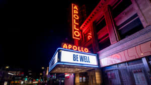 阿波羅劇院簷篷在夜晚發出紅藍光芒，帶有「BE WELL」訊息。