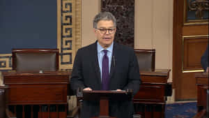 身穿西裝戴眼鏡的男子在木製講台上發言的正式會議廳。