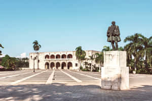 廣場上的雕像，前面是殖民地建築和棕櫚樹 — 建築 壁紙