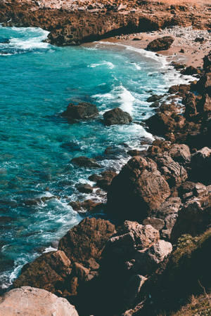 藍綠色的海浪拍打著岩石海岸，有沙灘。