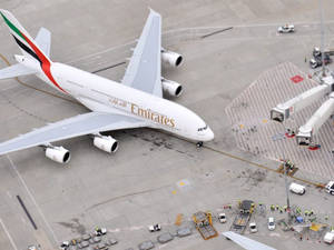 阿聯酋航空A380飛機停泊在機場閘口，有地勤人員和車輛。