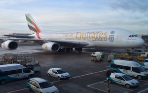 阿聯酋航空A380飛機停泊在機場閘口，有地面車輛。 — 倫敦 壁紙
