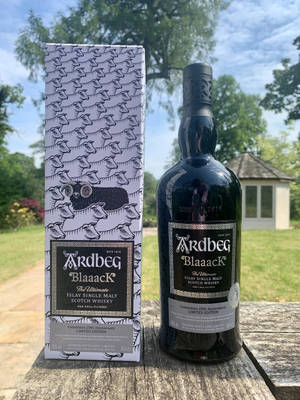 Ardbeg Blaaack威士忌瓶和盒子在戶外木桌上，配以綠意和天空。