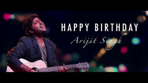 歌手Arijit Singh在舞台上彈結他，配有生日文字和彩色燈光。